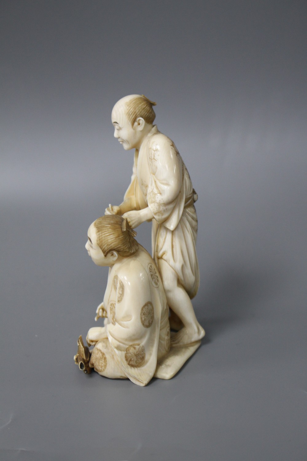 A Japanese Meiji period ivory okimono carved with a doctor treating a mans ear, signed, height 12cm